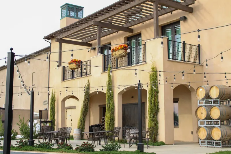 Warm stucco winery building with string lights and wine barrels